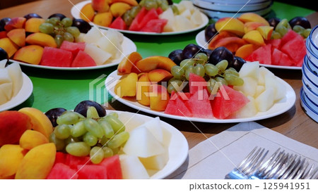 Fresh fruit plates featuring watermelon, peaches, grapes, and melon displayed on catering table, presenting vibrant, nutritious dessert selection for guests 125941951
