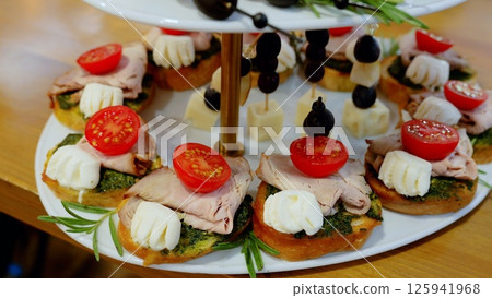 Gourmet canapes featuring pesto glazed pork, melting mozzarella, and vibrant cherry tomatoes artfully arranged on serving tray during upscale catering reception 125941968