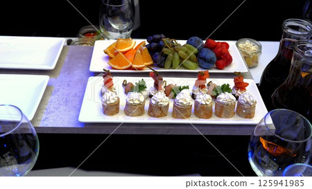 Small rolls filled with salmon and cream cheese arranged on a white rectangular plate, paired with fresh fruits and drinks for an enticing appetizer platter 125941985