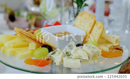 Rustic wooden board displaying artisan blue cheese, crisp crackers, ripe grapes, roasted walnuts, golden honey, and sweet dried apricots in elegant cheese platter arrangement 125942035