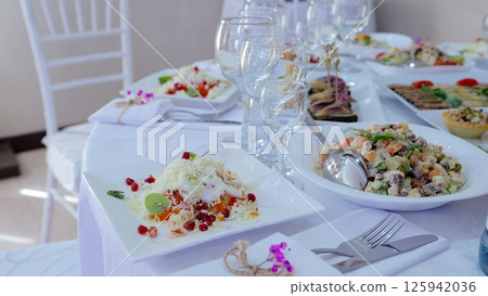Elegantly arranged dining table featuring gourmet salads, sprinkled with pomegranate seeds, garnished with fresh herbs, complemented by sleek wine glasses 125942036
