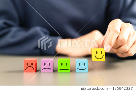 Customer satisfaction feedback survey concept. Person selects yellow smile face block from row of colorful blocks various facial expressions, different levels of customer satisfaction, feedback rating Customer satisfaction feedback survey concept. Person selects yellow smile face block from row of colorful blocks various facial expressions, different levels of customer satisfaction, feedback rating 125942327