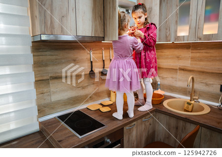 Two young girls enjoying a playful cooking adventure in a modern kitchen during a sunny afternoon Two young girls enjoying a playful cooking adventure in a modern kitchen during a sunny afternoon 125942726