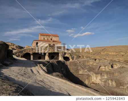 Church of uplistsikhe rising above the cave city ruins under a blue sky with white clouds Church of uplistsikhe rising above the cave city ruins under a blue sky with white clouds 125942843
