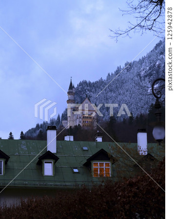 Majestic castle atop snowy mountains surrounded by quaint houses during twilight 125942878