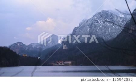 Scenic view of snow-capped mountains and a tranquil lake at dusk near a historical castle in Germany Scenic view of snow-capped mountains and a tranquil lake at dusk near a historical castle in Germany 125942883