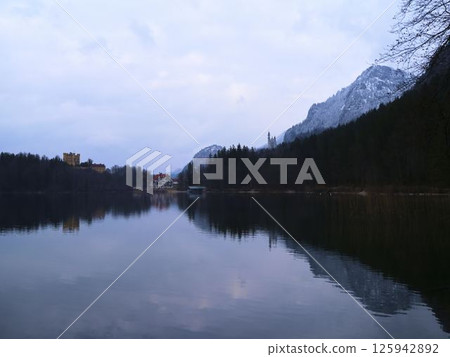 Serene lake view at dusk with mountain backdrop and reflections near a quiet village 125942892