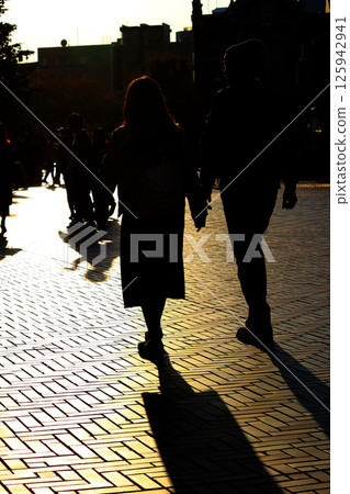 Silhouette of a couple walking through the city in the sunlight at dusk 125942941
