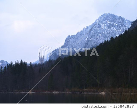 Snow-covered mountain landscape with a castle near a tranquil lake during winter dusk Snow-covered mountain landscape with a castle near a tranquil lake during winter dusk 125942957