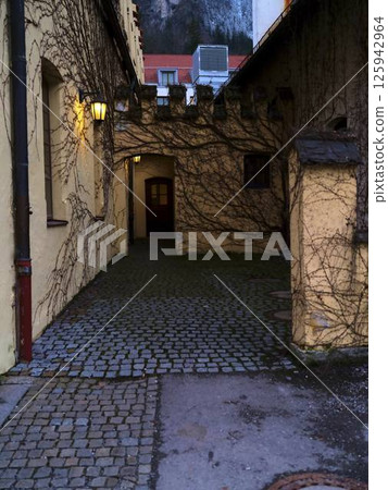 Stone pathway leads to secluded alley surrounded by ivy-clad walls in an old town during twilight hours 125942964