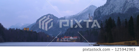 Majestic mountains surround a serene lake with a historic castle nestled in the landscape during twilight hours 125942965