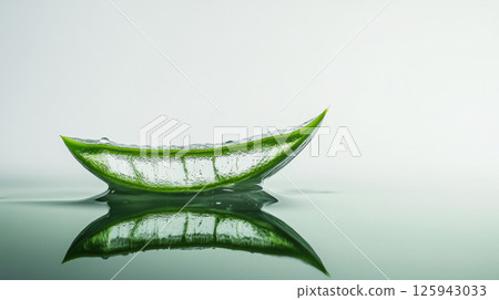 Fresh cut aloe vera leaf with one drop of gel ready to fall, on a white reflective surface. Copy space, 125943033