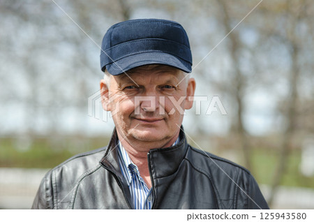 Pensioner in a hat with a visor, jacket and shirt on the street. In sunny weather, the pensioner is smiling and enjoying life. 125943580