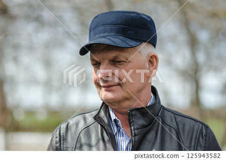 Pensioner in a hat with a visor, jacket and shirt on the street. In sunny weather, the pensioner is smiling and enjoying life. 125943582