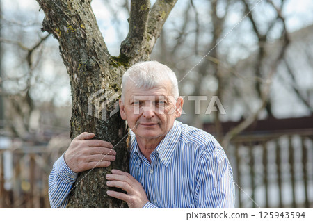The pensioner is leaning on a tree and smiling beautifully. An elderly man is leaning against a tree. The pensioner is leaning on a tree and smiling beautifully. An elderly man is leaning against a tree. 125943594