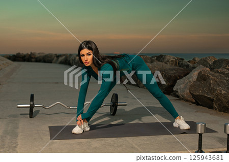 fitness enthusiast performs stretch on mat ocean showcasing determination health and exercise. Weights sit alongside workout area during sunset. fitness enthusiast performs stretch on mat ocean showcasing determination health and exercise. Weights sit alongside workout area during sunset. 125943681