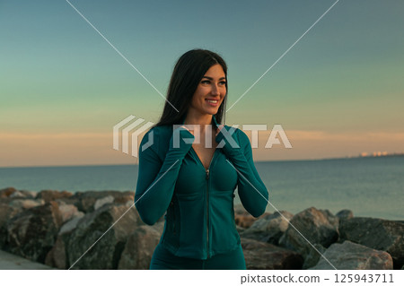 fit woman stands ocean joyful smile dressed in activewear and enjoys tranquil sunset while taking moment appreciate her surroundings. fit woman stands ocean joyful smile dressed in activewear and enjoys tranquil sunset while taking moment appreciate her surroundings. 125943711