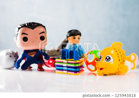 A yellow plastic fish is lying among other small toys. Next to it stands a plastic construction set boy dressed in a colorful costume. A yellow plastic fish is lying among other small toys. Next to it stands a plastic construction set boy dressed in a colorful costume. 125943818