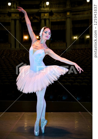 Ballet dancer in white tutu balancing on pointe on theater stage 125943837