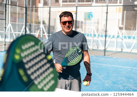 Man enjoys playing padel under the sun on a bright day. Man enjoys playing padel under the sun on a bright day. 125944464
