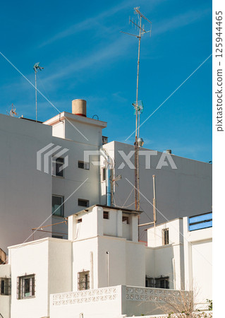 White urban architecture against a vibrant blue sky, featuring intricate rooftop structures. White urban architecture against a vibrant blue sky, featuring intricate rooftop structures. 125944465
