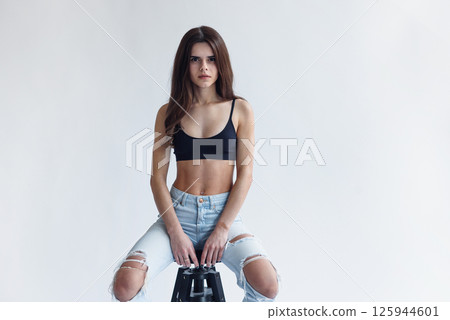 Charming skinny beautiful girl with perfect abs in jeans and black top isolated on gray background Charming skinny beautiful girl with perfect abs in jeans and black top isolated on gray background 125944601