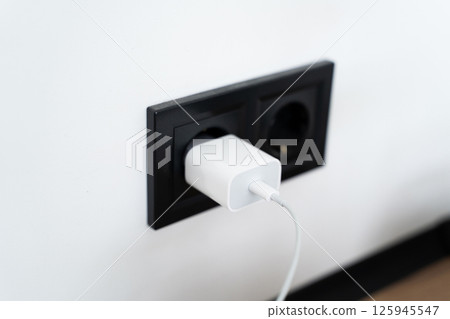 White USB charger plugged into black wall socket in modern interior 125945547