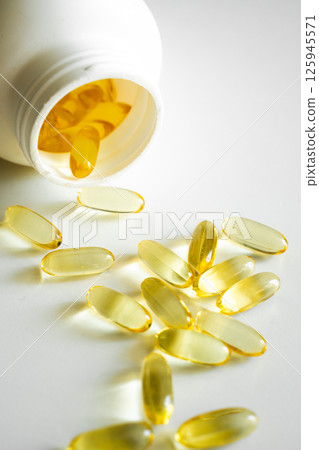 Fish oil capsules spilling from white bottle onto clean surface 125945571