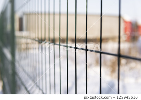 Industrial metal fence with blurred snowy background and semi-trailer truck on winter day Industrial metal fence with blurred snowy background and semi-trailer truck on winter day 125945616