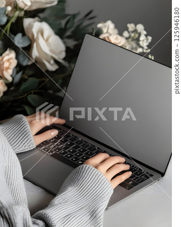 An open laptop stands on table with hands. Dark background. Side view. Computer mockup for design 125946180