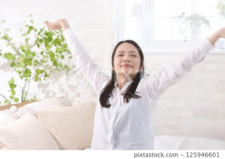 Middle-aged woman sitting on bed and stretching 125946601