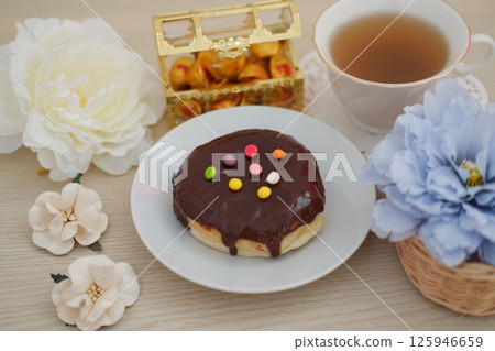 a chocolate-glazed donut with colorful candy sprinkles served on a white plate 125946659