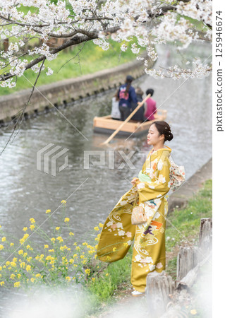 新河岸的櫻花盛開，櫻花下有一艘船穿過，還有一位身著和服的女子 125946674