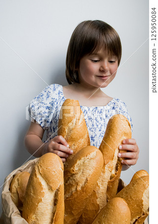 Young caucasian girl enjoying fresh bread in blue floral dress 125950084