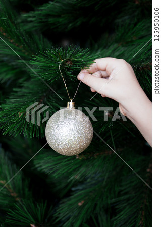 Childs hand decorating Christmas tree with glittering ornament 125950106