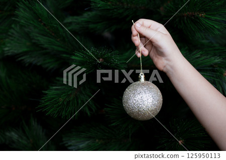 Childs hand hanging gold bauble on Christmas tree branch Childs hand hanging gold bauble on Christmas tree branch 125950113