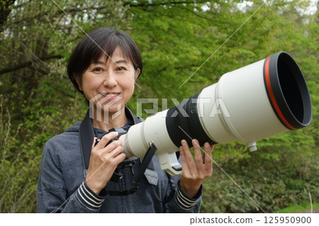 Smiling middle-aged woman holding a telephoto camera, looking at the camera Smiling middle-aged woman holding a telephoto camera, looking at the camera 125950900