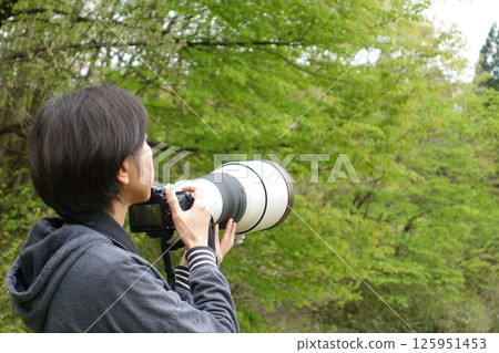 A woman holding a camera and searching for a subject - photographing wild birds 125951453