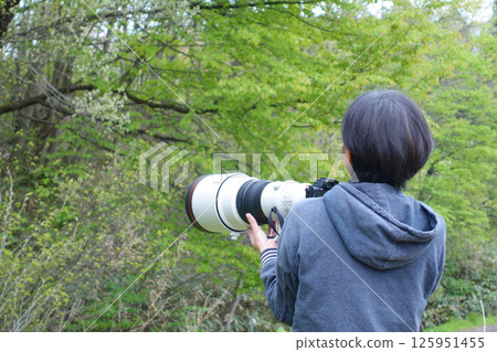 A woman holding a camera and searching for a subject - photographing wild birds A woman holding a camera and searching for a subject - photographing wild birds 125951455