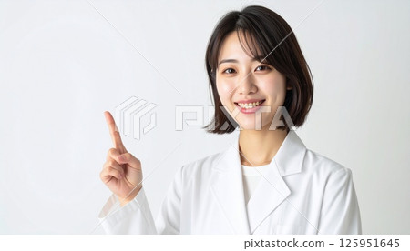 A young woman in a white coat pointing up A young woman in a white coat pointing up 125951645