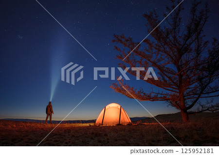 Silhouette of alone hiker man at his illuminated camp tent at starry night 125952181