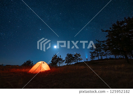 Small silhouette of alone hiker man at his illuminated camp tent at starry night Small silhouette of alone hiker man at his illuminated camp tent at starry night 125952182
