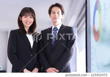 一位身穿西裝的男士和一位女士站在會議室的螢幕前 一位身穿西裝的男士和一位女士站在會議室的螢幕前 125952473