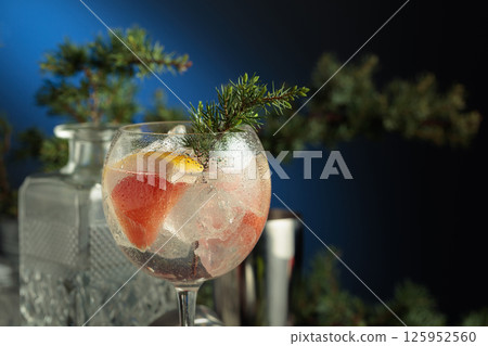 Cocktail gin and tonic with ice and pink grapefruit slices in wet glass on a dark blue background. 125952560