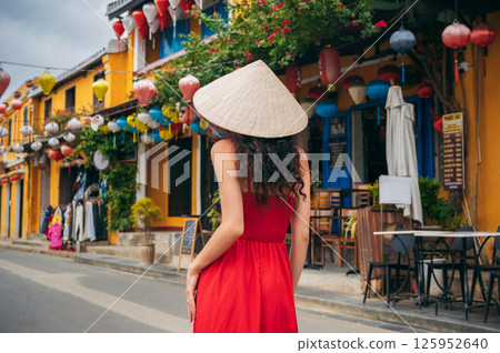 back of asian woman tourist in a traditional Vietnamese hat and red dress on the street in old town in Hoi An city in Vietnam in Asia 125952640