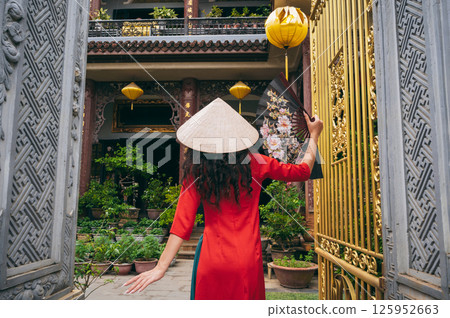back of a female traveler tourist in a Vietnamese hat at Buddhist temple in Hoi An in Vietnam in Asia 125952663