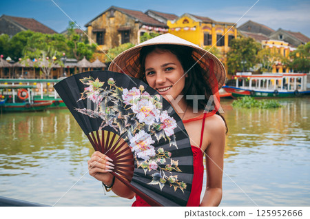 happy young female tourist traveler in Vietnamese hat with a fan on a bridge in Hoi An in Vietnam in Asia happy young female tourist traveler in Vietnamese hat with a fan on a bridge in Hoi An in Vietnam in Asia 125952666