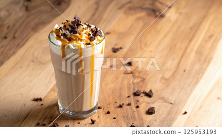 Creamy milkshake topped with whipped cream, chocolate shavings, and caramel drizzle on wooden table Creamy milkshake topped with whipped cream, chocolate shavings, and caramel drizzle on wooden table 125953193
