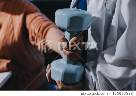 Physiotherapist training with patient using dumbbells in clinic,Physical therapy concept 125953588