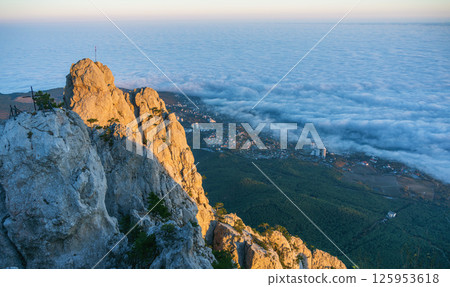 Morning landscape with rocky mountains, cliffs, and clouds lying below Morning landscape with rocky mountains, cliffs, and clouds lying below 125953618